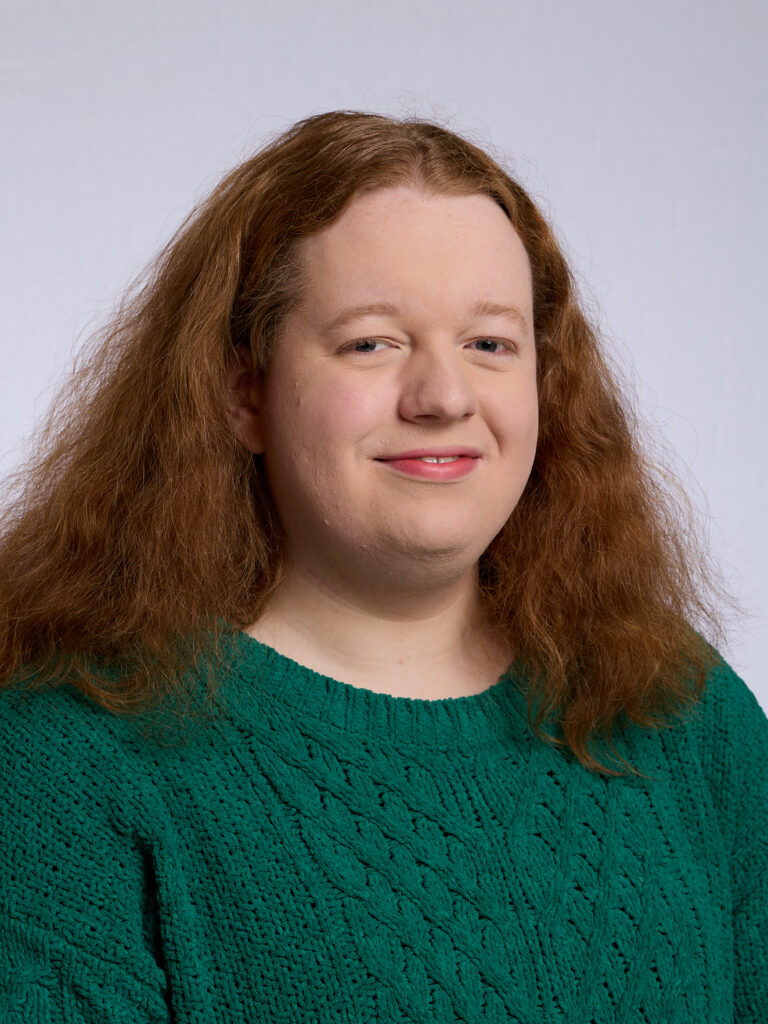 A headshot of Olivia looking towards the camera wearing a green jumper